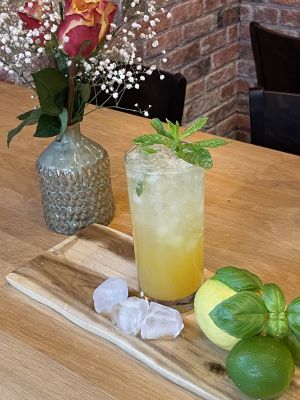 Frischer Cocktail mit Minze, Zitrone und Basilikum, dekoriert mit Blumen auf einem Tisch.