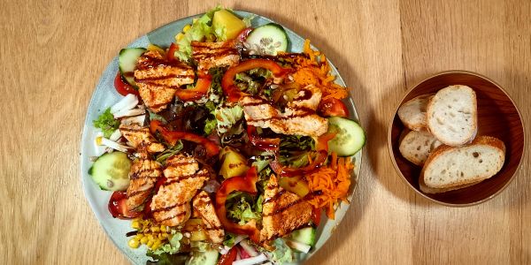 Salatteller mit gegrilltem Hähnchen, Gemüse und Brot.