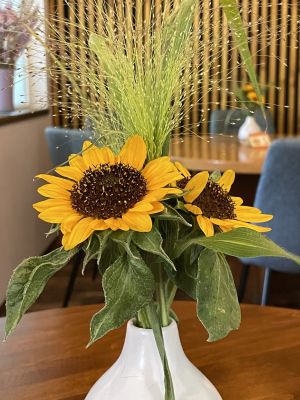 Sonnenblumenstrauß in weißer Vase auf einem Tisch, mit dekorativem Hintergrund.