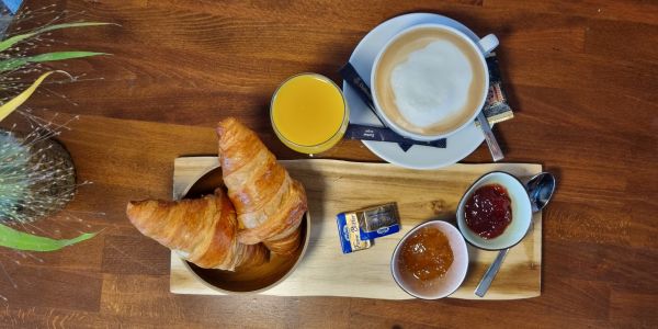 Frühstück mit Croissants, Marmelade, Orangensaft und Kaffee auf einem Holztablett.