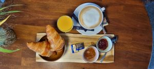 Frühstück mit Croissants, Marmelade, Orangensaft und Kaffee auf einem Holztablett.