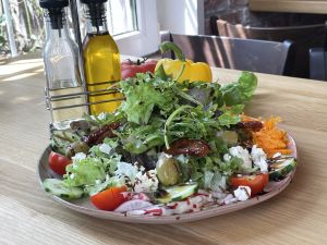 Bunter Salat mit Oliven, Feta und Gemüse, dekoriert mit Ölflaschen und Paprika.