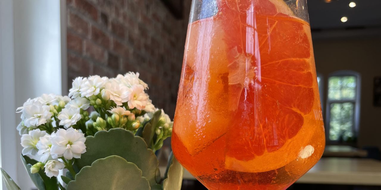 Aperitif mit Orangenscheibe und Blume auf Tisch im Restaurant, rustikale Atmosphäre.