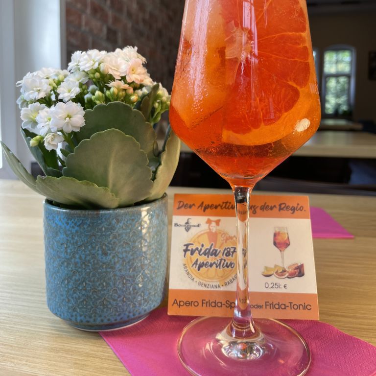 Aperitif mit Orangenscheibe und Blume auf Tisch im Restaurant, rustikale Atmosphäre.