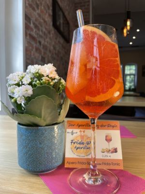 Aperitif mit Orangenscheibe und Blume auf Tisch im Restaurant, rustikale Atmosphäre.