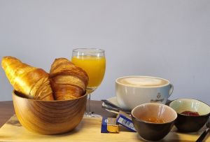 Frühstück mit Croissants, Kaffee, Orangensaft und Marmelade auf einem Holztablett.