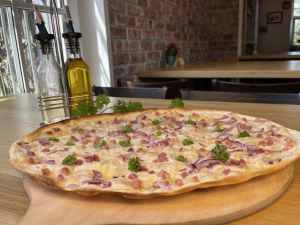 Flammkuchen mit Speck und Zwiebeln auf Holzbrett, dekoriert mit Petersilie und Ölflaschen.