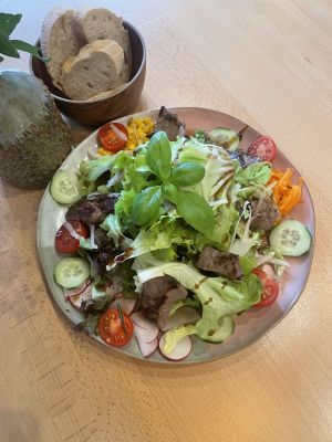 Bunter Salatteller mit Steakstreifen, frischem Gemüse und Baguette im Hintergrund.